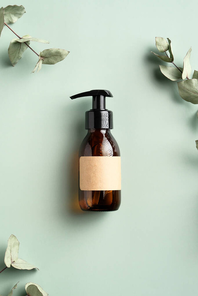 Dark amber glass dispenser bottle with homemade shampoo and eucalyptus leaves on green background. SPA natural organic cosmetic product packaging design, branding. - Photo, Image