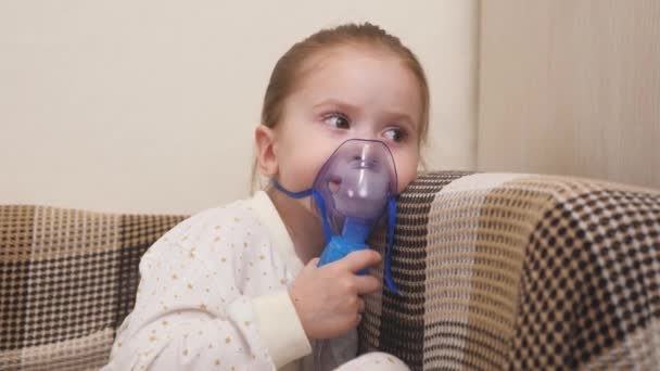 Ένα χαριτωμένο μωράκι με μάσκα αναπνέει από έναν εισπνευστήρα. Εισπνοή κατ 'οίκον. Το παιδί λαμβάνει αναπνευστική θεραπεία με νεφελοποιητή. Περιποιήσου το παιδί από τον κορωνοϊό στο σπίτι. Ένα κοριτσάκι. - Πλάνα, βίντεο