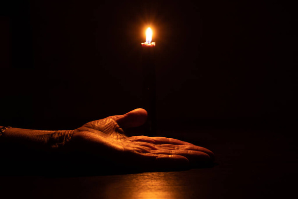 wyciągnięta dłoń starszej kobiety przy płomieniu świecy w ciemności - Zdjęcie, obraz