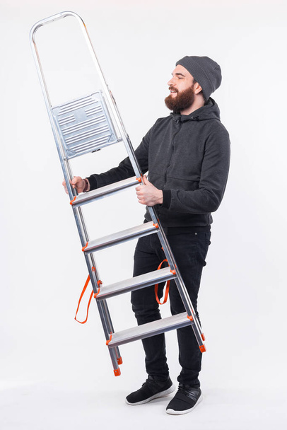 Full length photo of bearded man holding portable metal stairs - Foto, Imagen