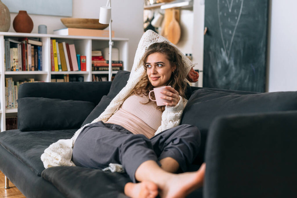 woman relaxed sitting on sofa in her home and drinking morning coffee - Foto, Imagem