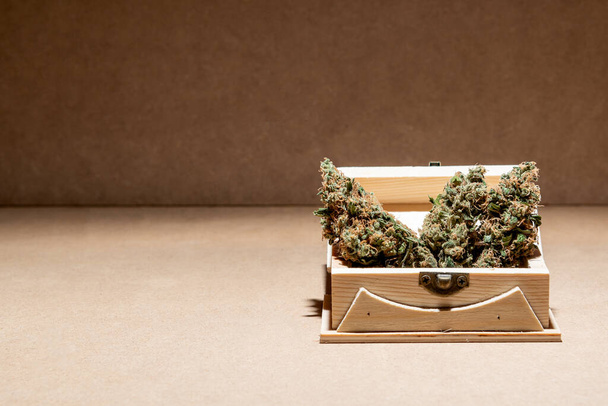 Details van enkele medicinale marihuana knoppen klaar voor consumptie in een houten doos. Selectieve focus op bruine achtergrond. - Foto, afbeelding