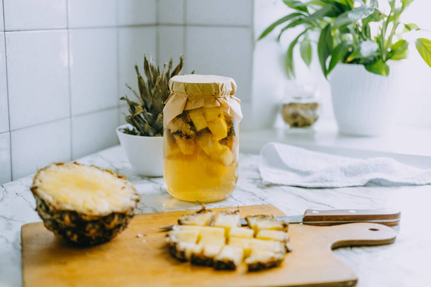 Fermented pineapple kombucha drink tepache. Cooking process of homemade probiotic superfood pineapple beverage. Drink jar and sliced pineapple on home kitchen - Photo, Image