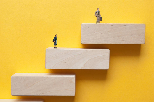 Miniature woman and man standing on wooden steps on different levels  - 写真・画像