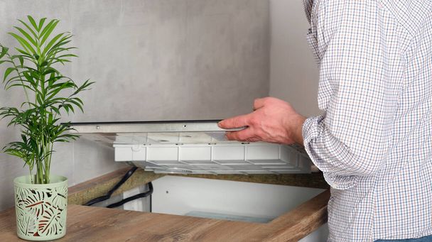 Ein junger Reparateur installiert ein schwarzes Induktionsherd in einer modernen weißen Küche im skandinavischen Stil mit Betonwand. Elektriker, mach 's selbst. Hausarbeit.  - Foto, Bild