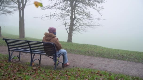 Laaja kuva surullisesta vanhuksesta, joka istuu yksin puistossa sumuisena aamuna. - Materiaali, video