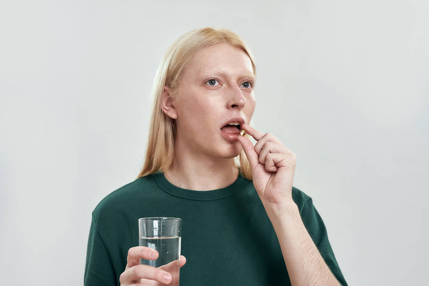 Young caucasian man swallowing pill with water - Foto, immagini