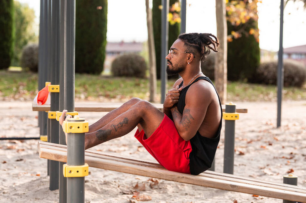 Молодой человек делает приседания во время тренировки в парке гимнастики на улице тренировки - Фото, изображение