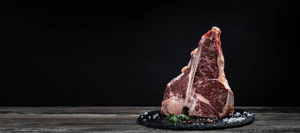 ωμό φιλέτο porterhouse ή Fed T Bone Steak ξηρά παλαίωση του βοείου κρέατος Έτοιμο να μαγειρέψουν σε ξύλινο πίνακα με βότανα, πιπέρι και αλάτι. - Φωτογραφία, εικόνα