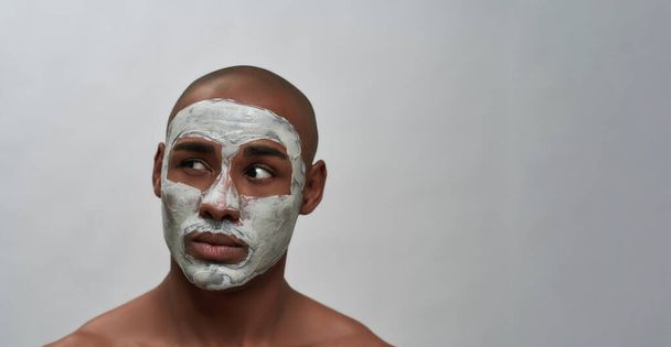 Handsome young african american man looking aside, using facial blackhead removal mask, posing isolated over gray background - Photo, image