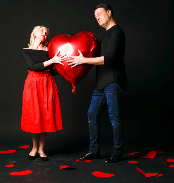 A girl and a guy hold a heart balloon inflatable valentine, happiness flirt, on the floor hearts are a beautiful layout. the formula for the occasion. love forever, frame in red dress girl, barefoot - Valokuva, kuva