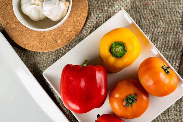 Tahta kesme tahtasında domates ve kasede sarımsak rengarenk biberlerin yakın plan çekimi. - Fotoğraf, Görsel