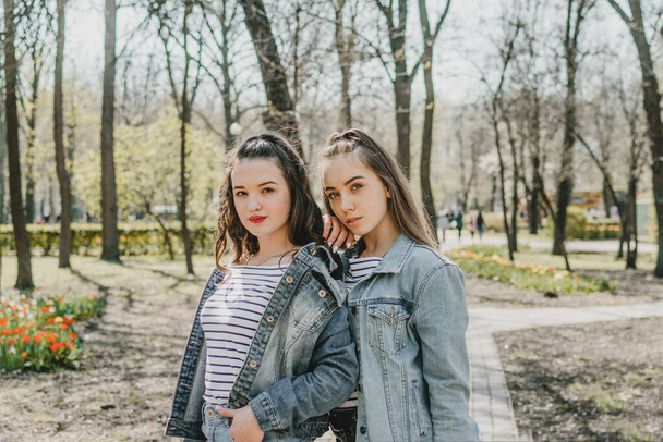 Gen z girls enjoying outdoors, expressing positive emotions. Outdoor photo of two girl friends having fun in the park. Two happy joyful young women jumping and laughing together - Photo, Image