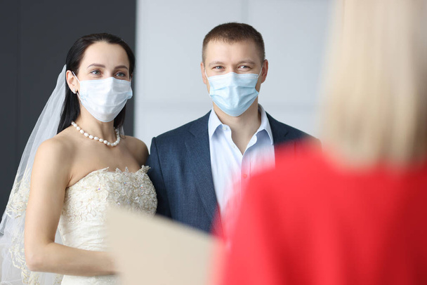 Άνδρας και γυναίκα με γαμήλια κοστούμια και ιατρικές προστατευτικές μάσκες κατά την τελετή - Φωτογραφία, εικόνα