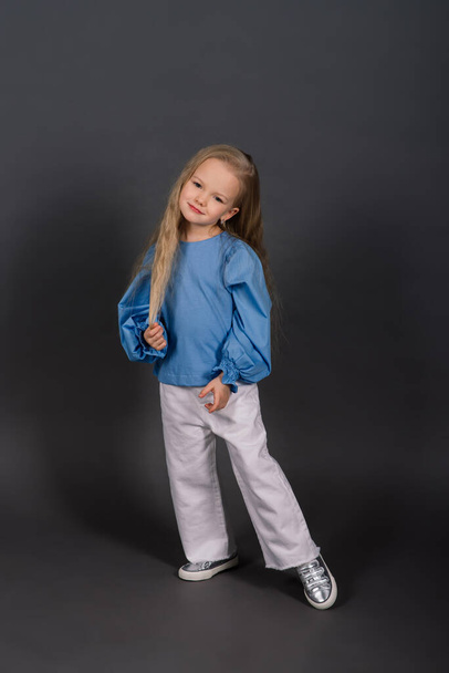 Little blonde girl, she laughing, sitting on floor, posing isolated on blue. Childhood, fashion, advertising and sport. Close up, copy space - Photo, Image