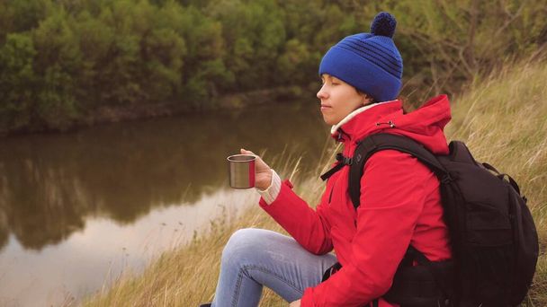 The girl drinks tea from a mug sitting on a high mountain and enjoying nature in the park. Woman traveler looking for adventure. Relax on the hike. Long distance hiking trips. Human explorer of - Photo, Image