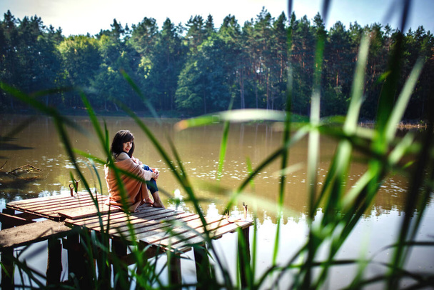 Krásná dívka s dlouhými brunetovými vlasy sedí na mostě. příroda. - Fotografie, Obrázek