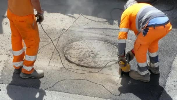 Drilling works on the road, workmen in orange uniform working on construction site on the sidewalk. Male professional workers using powerful cutting machine for breaking old layer of cement and - Footage, Video