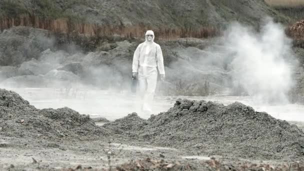 Τεχνικός εργαστηρίου με μάσκα και στολή χημικής προστασίας, περπατά σε στεγνό έδαφος με μια εργαλειοθήκη μέσα από τοξικό καπνό - Πλάνα, βίντεο