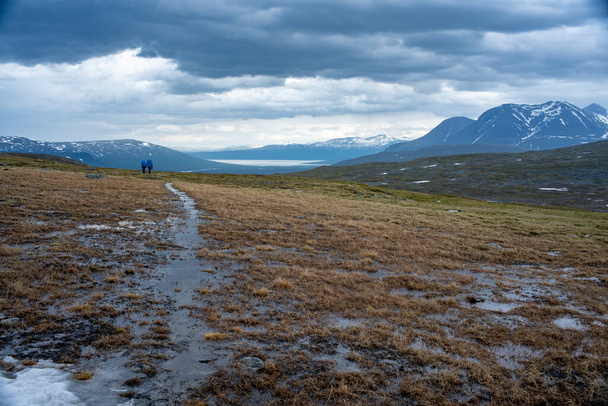 Padjelanta National Park Panorama Mountain landscape with Wet Hiking Trail leading away from Camera to a group of friends trekking and Akka Mountain. - Photo, Image