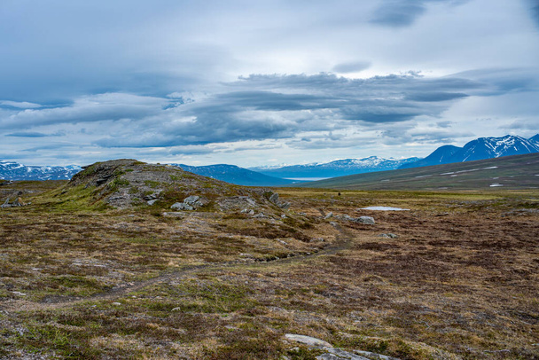 Padjelanta National Park Panorama Mountain landscape with Wet Hiking Trail leading away from Camera to a group of friends trekking and Akka Mountain. - Fotografie, Obrázek