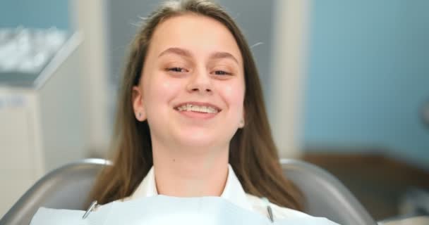 Diş muayenehanesinde diş teli takan neşeli bir kızın portresi. - Video, Çekim
