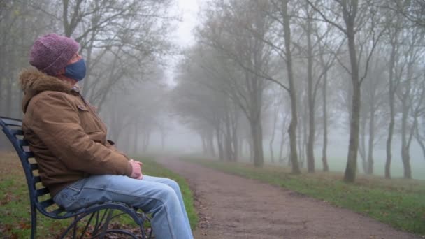 Un tiro medio de un triste anciano sentado solo en un parque en una mañana brumosa - Metraje, vídeo