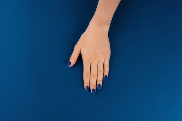Weibliche Hände mit Maniküre von klassischer blauer Farbe auf blauem Hintergrund - Foto, Bild