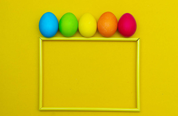 Закрашенные яйца на жёлтом фоне. Куриные яйца на желтом фоне в рамке. Пространство для текста. Куриные яйца цветные. Пасха. Православный праздник. Статья о Пасхе. Статья о пользе и вреде яиц. Принято. Желтый фон - Фото, изображение