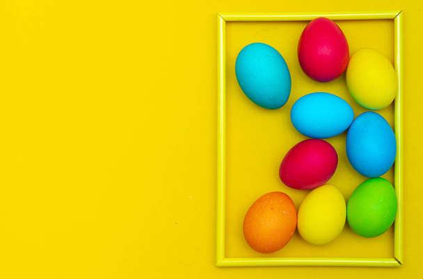 Painted eggs on a yellow background. Chicken eggs on a yellow background in a frame. Space for the text. Chicken eggs are colored. Easter. Orthodox holiday. An article about Easter. Article about eggs benefits and harms. Copy space. Yellow background - Photo, Image