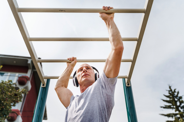 Adult caucasian man training outdoor - Male athlete in his daily routine train on bars in park in sunny spring or summer day - Real people health and fitness street workout concept - Photo, Image