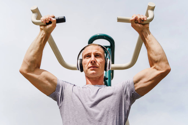 Adult caucasian man training outdoor in sunny spring or summer day - Male athlete in his daily routine train shoulders on machine in park - Real people health and fitness street workout concept - Photo, Image