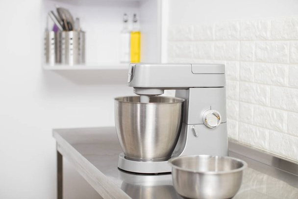 Small Electric Kitchen Appliances. Modern silver kitchen stand mixer in light cozy confectionery. A closeup of Multi-Task Blender mixing dough, and Stainless Steel bowl on the table - Foto, Imagem