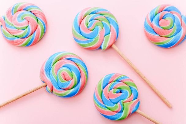 Colorful lollipops swirls on sticks. Striped spiral multicolored candy on pink background, top view - Photo, Image