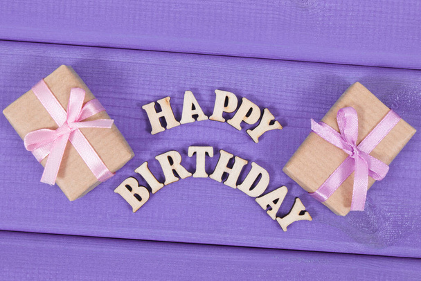 Wrapped gifts with ribbon for birthday. Inscription happy birthday on purple boards - Фото, изображение