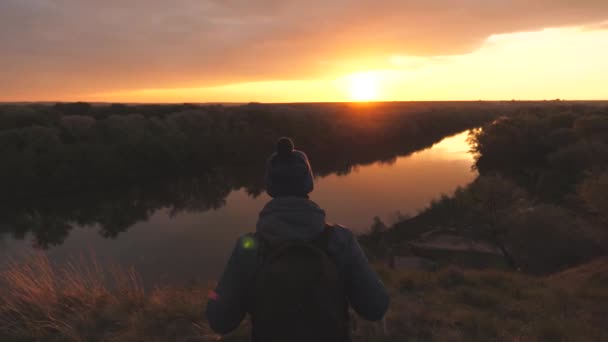 A man traveler walks along the road with a backpack on his shoulders at sunset in the sky and raises his hands up. Rejoice at victory. A tourist trip to the future at dawn. Search for adventure and - Footage, Video