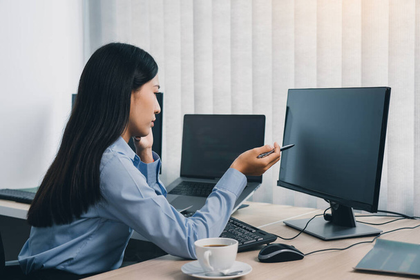Mujer asiática concentrada lluvia de ideas mientras codifica datos en PC de escritorio mientras trabaja en códigos de computadora en la oficina. - Foto, imagen