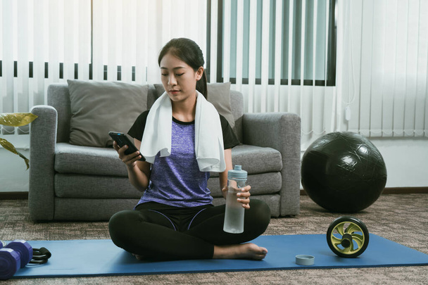 Ázsiai nő játszik smartphone otthon szünet alatt jóga gyakorlat és ivás édesvíz. - Fotó, kép