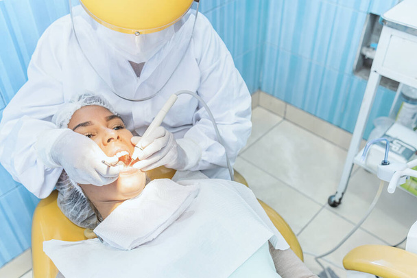 Słodka kobieta siedzi na krześle dentystycznym, podczas gdy dentysta bada jej zęby. Skupienie selektywne. - Zdjęcie, obraz