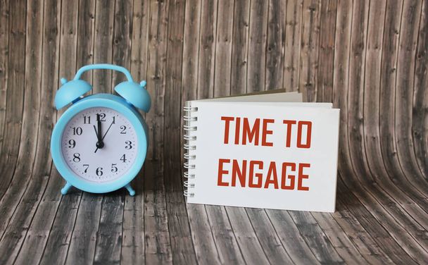 Tekst, het woord Time To Engage staat geschreven in een notitieboekje liggend op een houten tafel met een wekker. Bedrijfsconcept - Foto, afbeelding