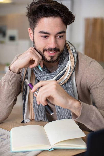 close up portrait of young man writing on notebook - Photo, image