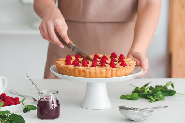Mujer cortando sabroso pastel de frambuesa en la cocina, primer plano - Foto, imagen