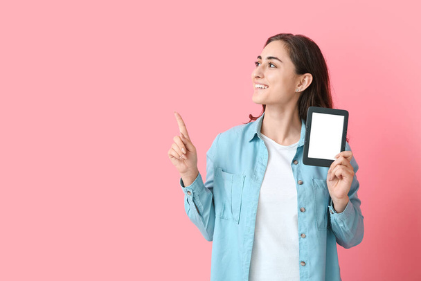Jeune femme avec e-reader pointant quelque chose sur fond de couleur - Photo, image