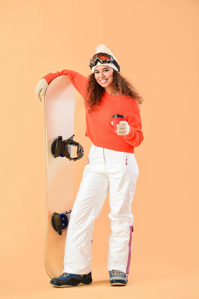 Female snowboarder drinking coffee on color background - Fotó, kép