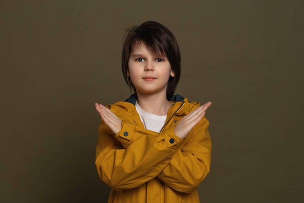 Niño serio en ropa casual mirar manteniendo dos brazos cruzados, concepto de negación. Estudio de tiro, fondo verde - Foto, Imagen