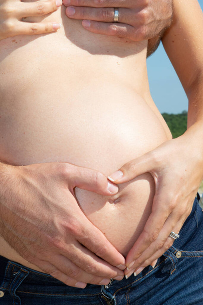 έγκυος γυναίκα και ο άνθρωπος αγκαλιάζει γυμνό τόπλες κοιλιά με τα χέρια υπαίθρια - Φωτογραφία, εικόνα