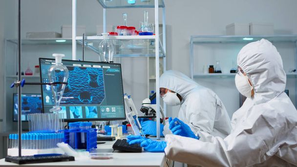 Naukowiec w kombinezonie ppe trzymający probówkę z niebieskim płynem w sterylnym laboratorium - Zdjęcie, obraz