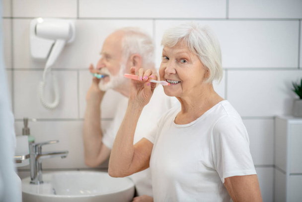 Elderly couple brushing their teeth together and looking contented - Foto, afbeelding