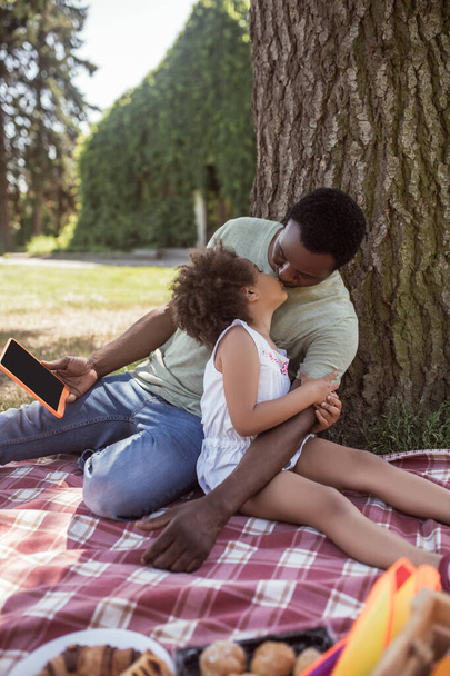 African american man and his cute kid having picnic in the park and feeling happy - Photo, Image