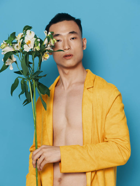 Sexy muž s nahým tělem na modrém pozadí a žlutý kabát s kyticí květin ve svátcích dárky - Fotografie, Obrázek